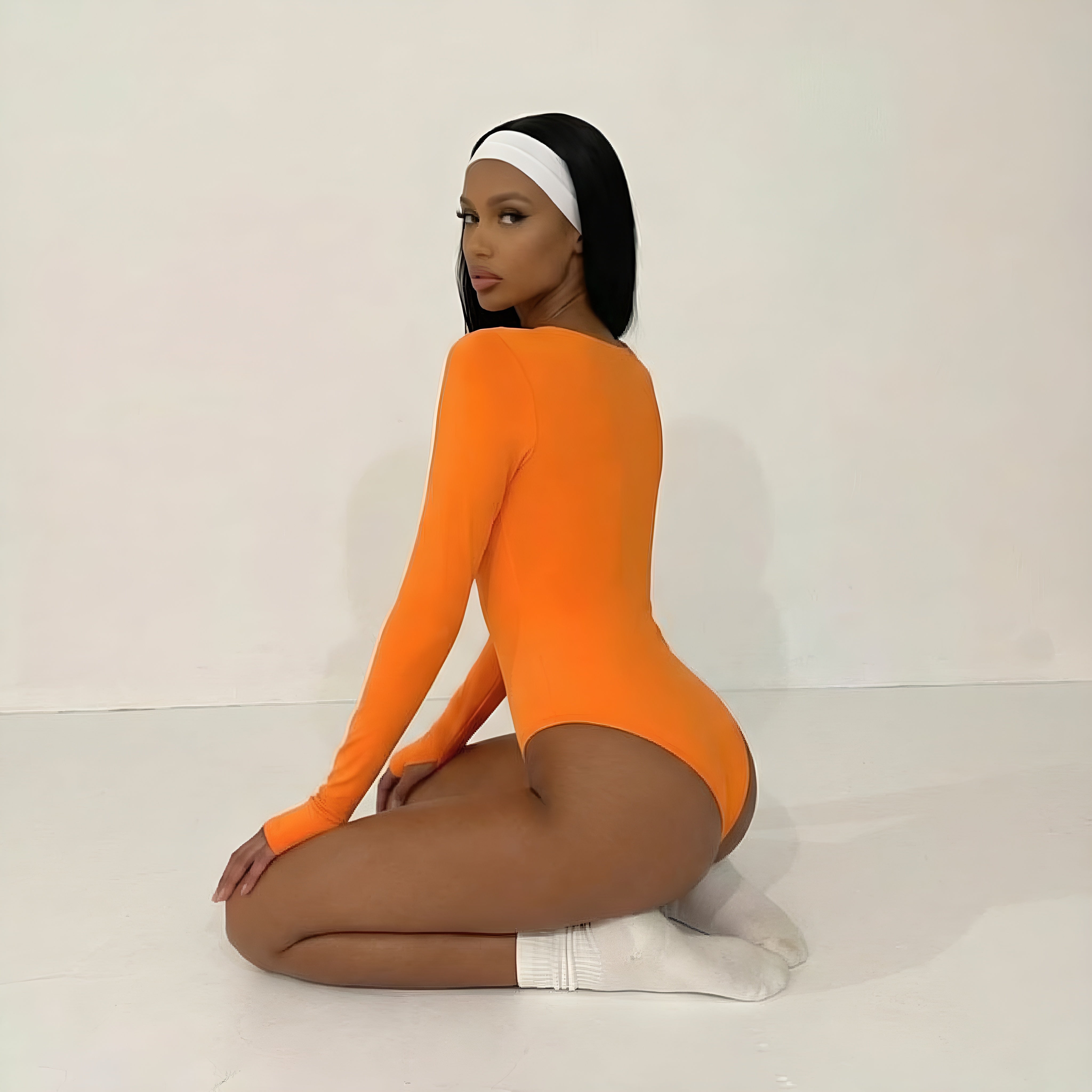 Person wearing an orange bodysuit sitting on a white floor with a plain background. Shapewear womans bodysuit lyvia.